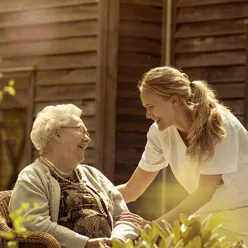 Eldre dame og sykepleier ute i en hage.