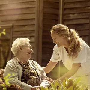 Eldre dame og sykepleier ute i en hage.
